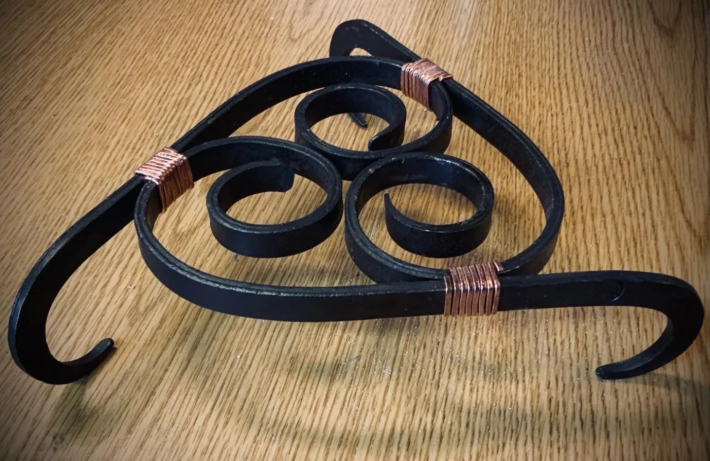 A forged trivet of scrolled iron, bound with copper wire